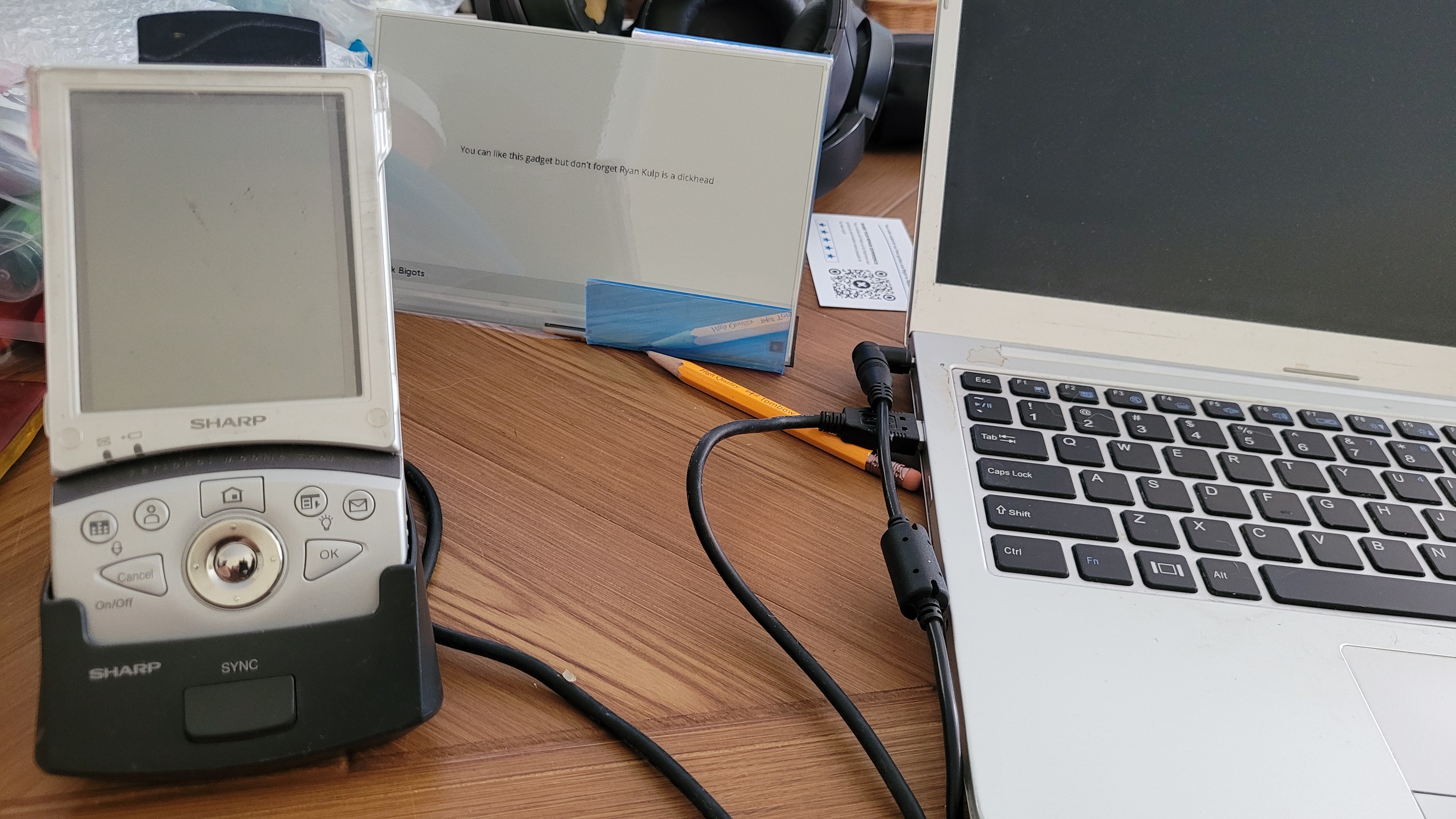 Sharp Zaurus sitting in a charging cradle that is plugged in to a laptop.